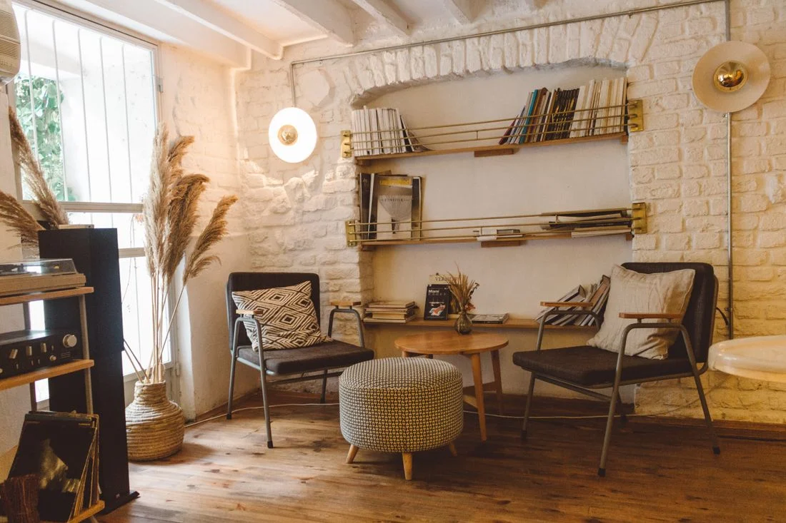 Two wooden armchairs and an ottoman beside open shelves