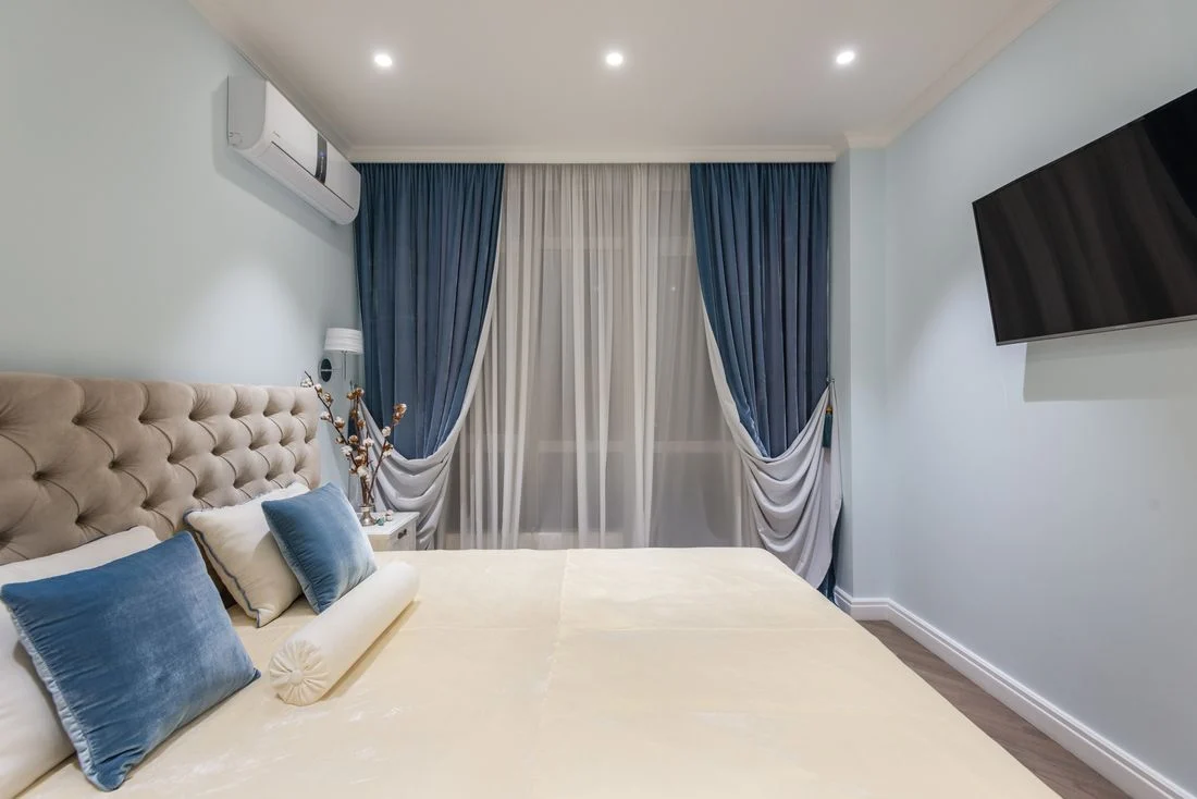 Bedroom with blue curtains, upholstered bed, and pale walls