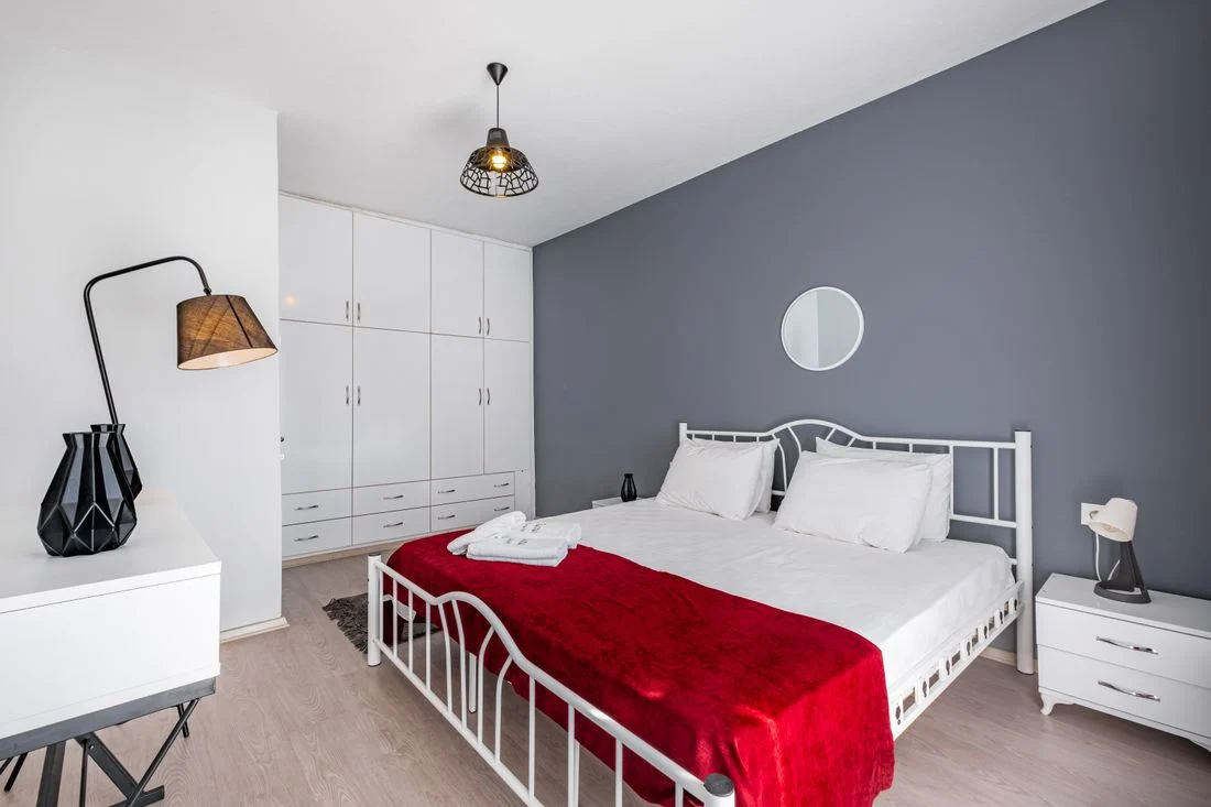 White bedroom with a red blanket and gray accent wall