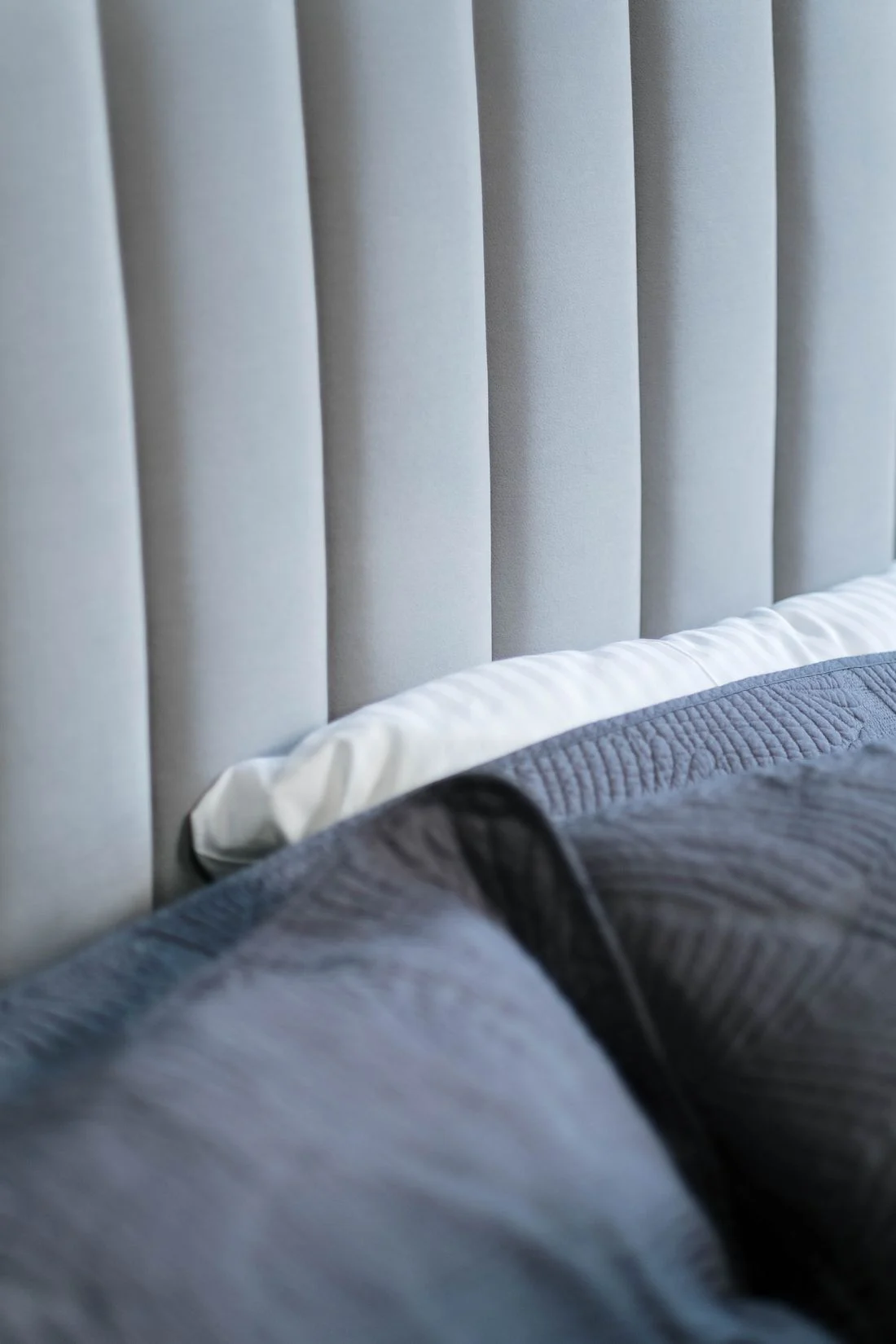 Close view of an upholstered headboard and gray bedding