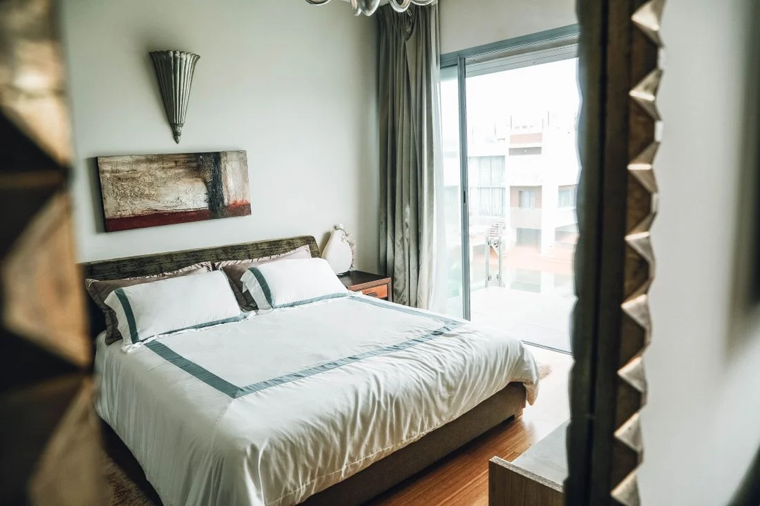 Made bed and bedside furnishings near a tall window