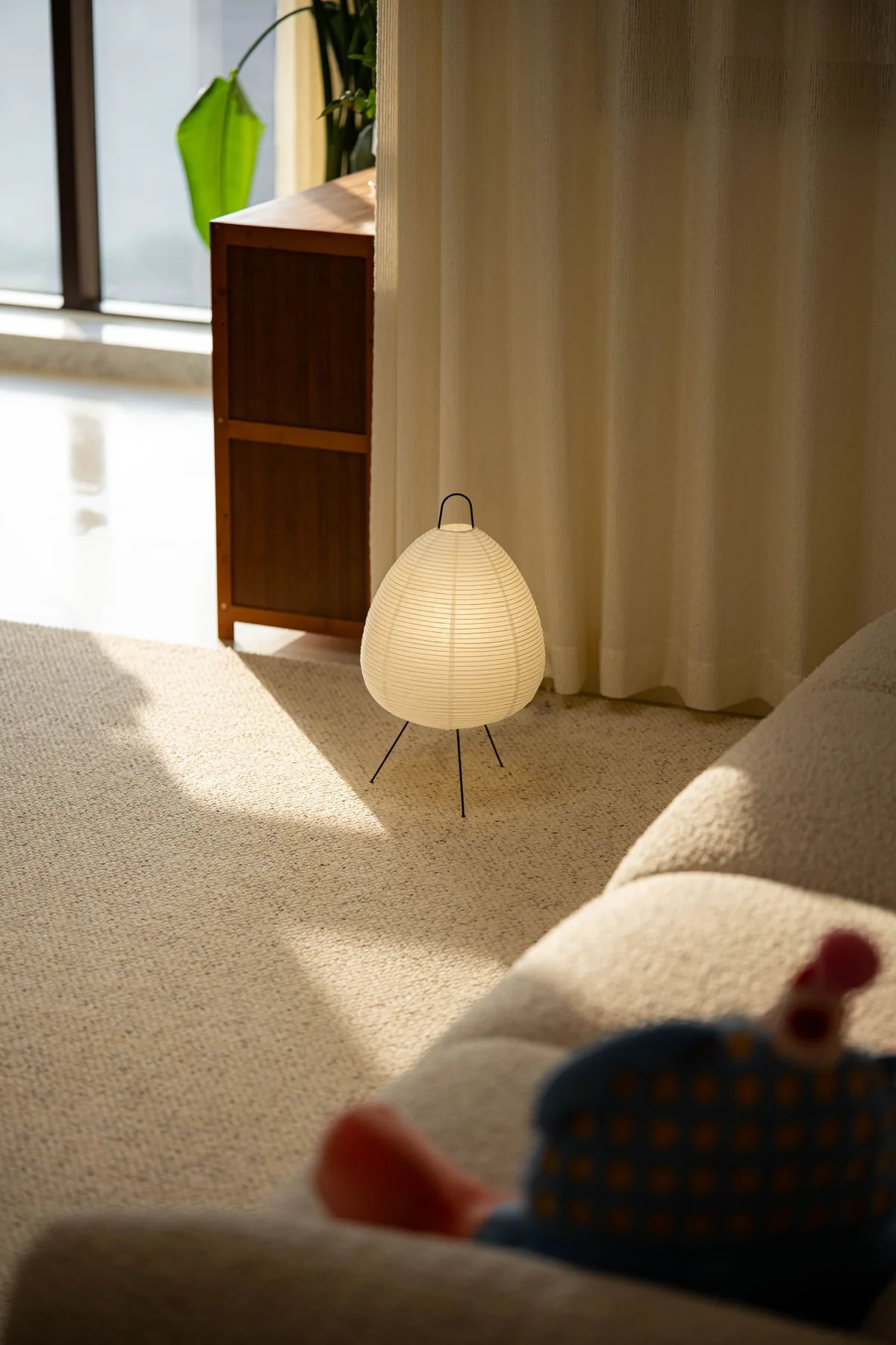 Glowing paper-shaded floor lamp beside a sofa and sheer curtains