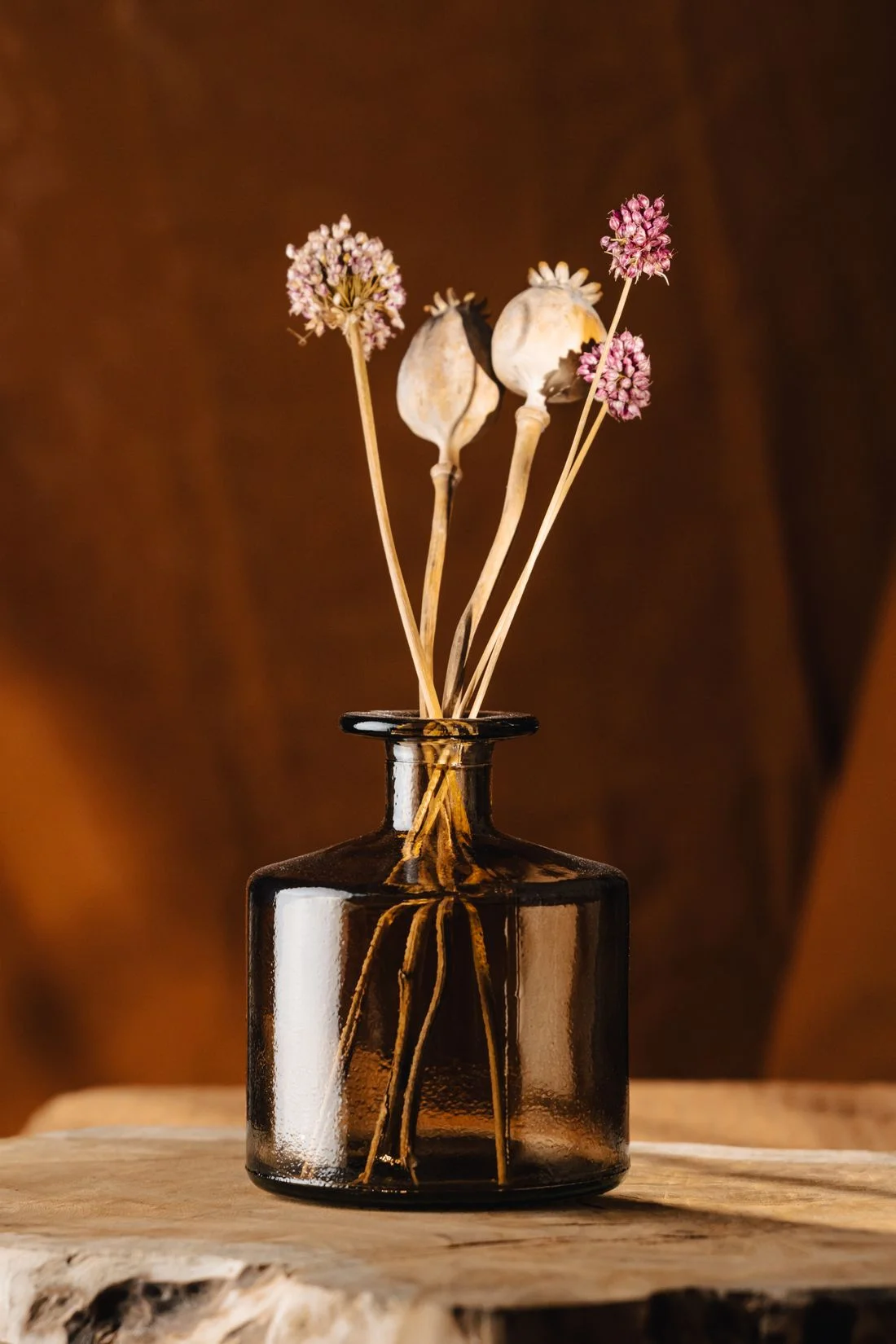 Dried stems in a brown glass vase